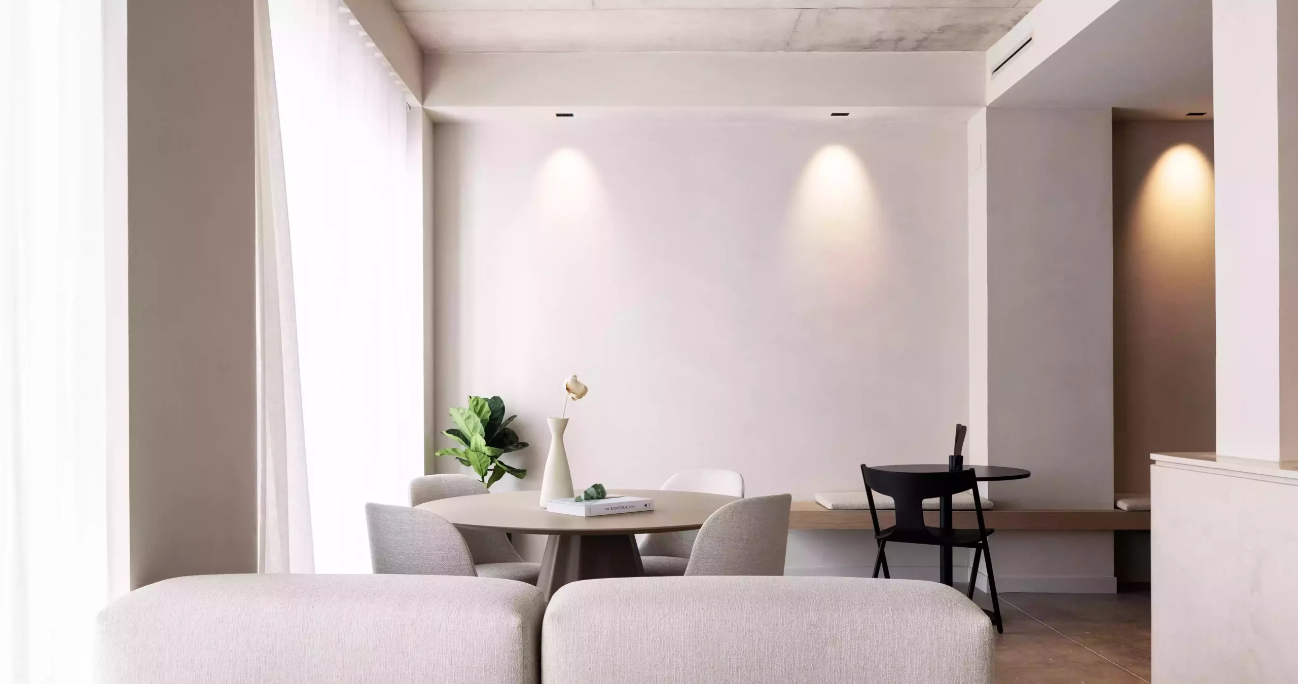 Salón minimalista del Yours Boutique Hotel en Valencia, con suelo de cemento pulido, techo de hormigón visto, mobiliario sencillo en tonos neutros y una planta decorativa central. | E6A